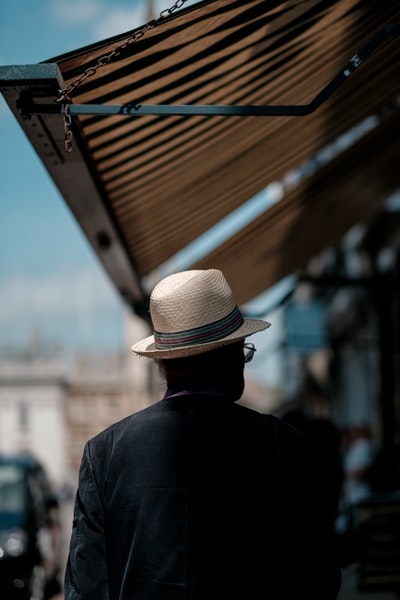 一名男子戴着白色草帽和黑色衬衫在街上行走
